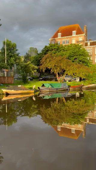 A serene scene of boats on a calm body of water with a house and trees in the background under a cloudy sky
